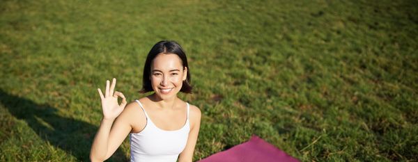 Portrait of asian woman sitting on rubber mat meditating showing okay sign